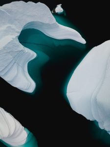 Aerial image of partially submerged icebergs in teal water so dark it's almost black.